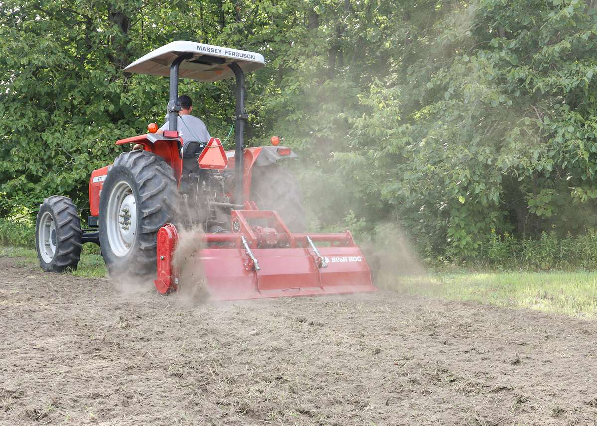 Photo of staff operating the tractor with rototiller for tree planting prep.