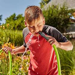 Image of a child drinking water out of a garden hose.